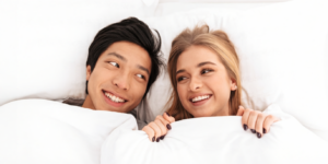 een jongen en een meisje liggen in bed en kijken elkaar aan terwijl ze glimlachen