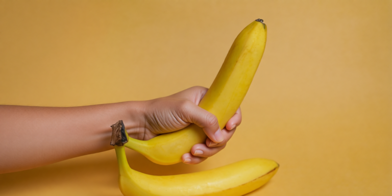 een hand houdt drie gele bananen vast tegen een gele achtergrond