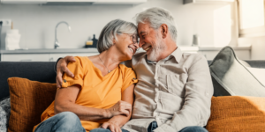 een oudere vrouw en man zitten op een bank en lachen terwijl ze hun voorhoofden tegen elkaar drukken