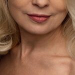close-up van de mond en hals van een vrouw met blond haar en roze lippenstift