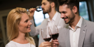 een vrouw en man glimlachen terwijl ze rode wijn drinken, met een andere man op de achtergrond