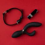 zwarte anusplug, riem en lippenstift op rode achtergrond