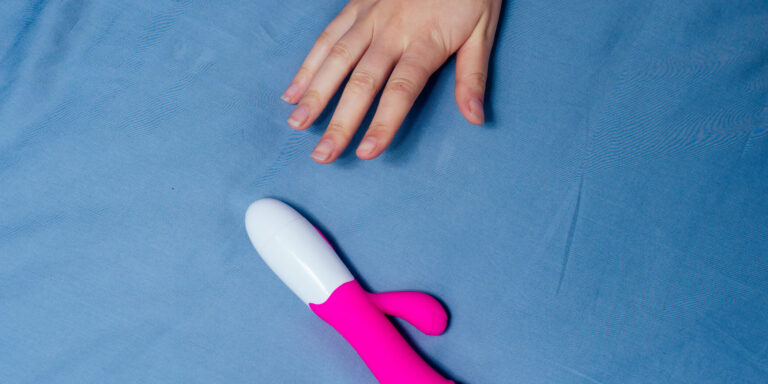 een hand ligt naast een roze en witte vibrator op een blauw oppervlak