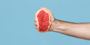 een hand knijpt in een halve grapefruit tegen een blauwe achtergrond