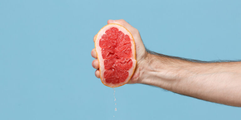 een hand knijpt in een halve grapefruit tegen een blauwe achtergrond