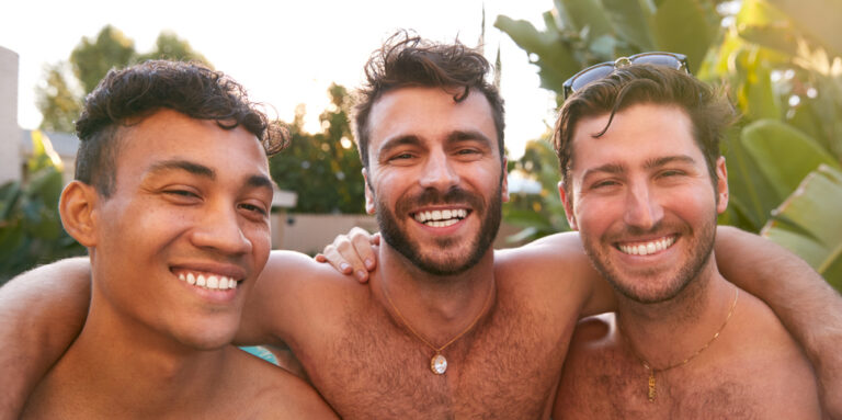 drie naakte mannen glimlachen naar de camera met armen om elkaars schouders
