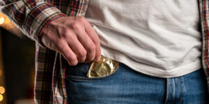 een man in een geruit overhemd en jeans steekt een gouden condoom in zijn broekzak