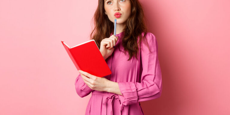 vrouw in roze jurk houdt rode notitieboekje vast en pen bij lippen tegen roze achtergrond
