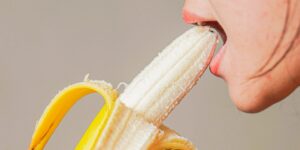 een vrouw bijt in een rijpe banaan, lippen open en tanden zichtbaar terwijl ze de vrucht vasthoudt