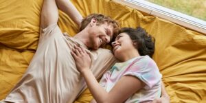 een man en vrouw lachen terwijl ze op een bed met gele lakens liggen
