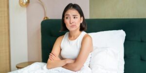 vrouw zit in bed met gekruiste armen en een ontevreden uitdrukking